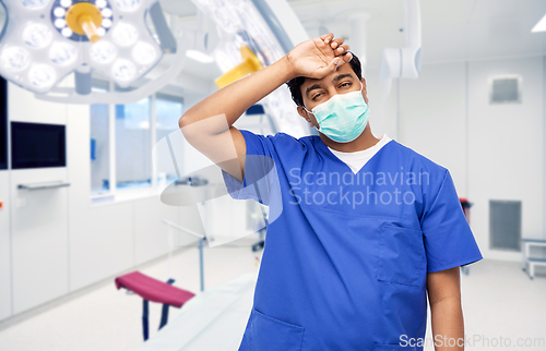 Image of tired indian male doctor in blue uniform and mask