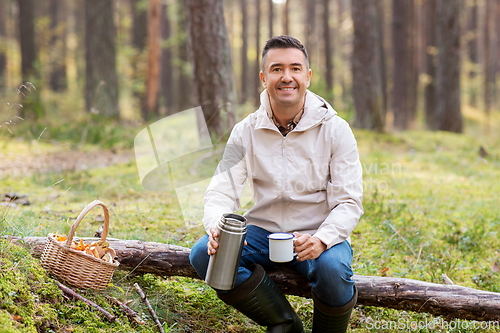 Image of man with basket of mushrooms drinks tea in forest