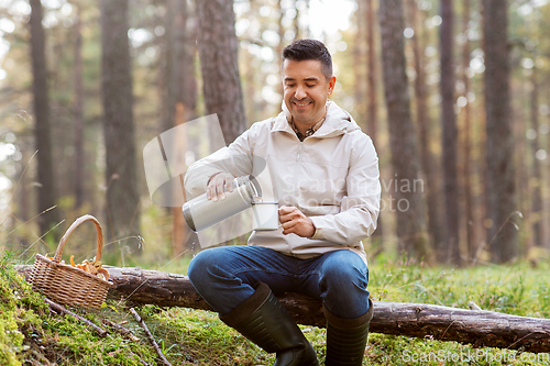 Image of man with basket of mushrooms drinks tea in forest