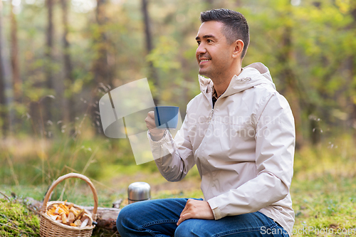 Image of man with basket of mushrooms drinks tea in forest