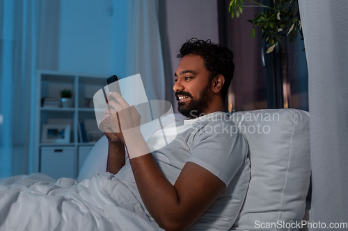 Image of indian man with smartphone in bed at home at night