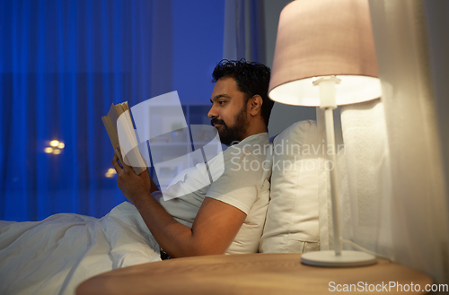 Image of indian man reading book in bed at night