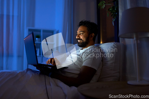 Image of indian man with laptop in bed at home at night