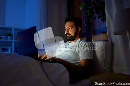 Image of indian man with laptop in bed at home at night