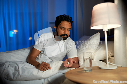 Image of indian man with medicine and water in bed at night