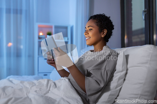 Image of woman with tablet pc in bed at home at night