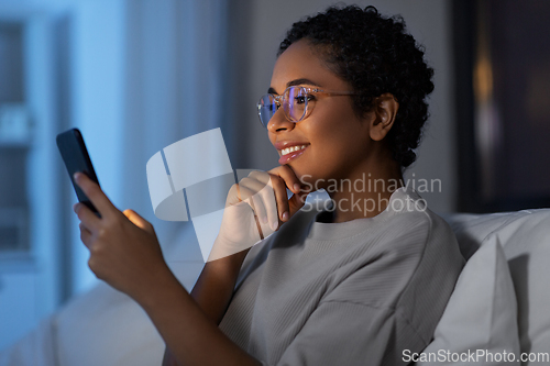 Image of african woman with smartphone in bed at night