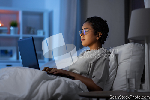 Image of woman with laptop in bed at home at night