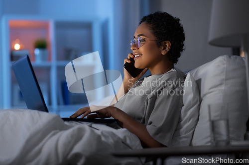 Image of woman with laptop calling on phone in bed at night