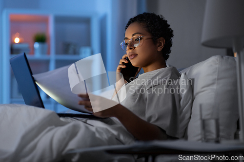 Image of woman with papers calling on phone in bed at night