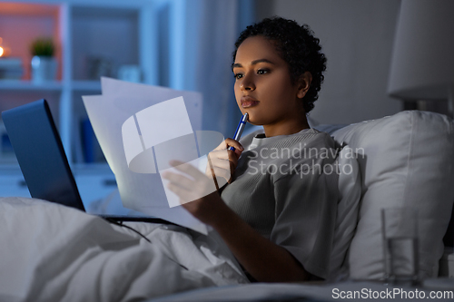 Image of woman with laptop and papers in bed at night