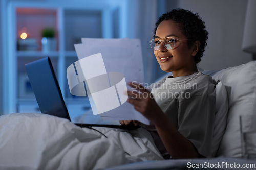 Image of woman with laptop and papers in bed at night