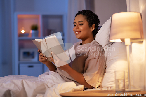 Image of smiling young woman reading book in bed at home