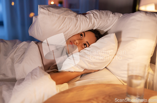 Image of angry african woman lying in bed and closing ears