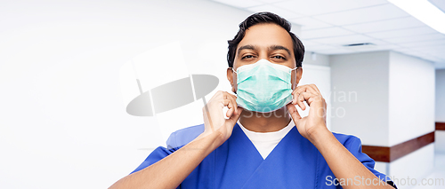 Image of indian male doctor in blue uniform putting mask on