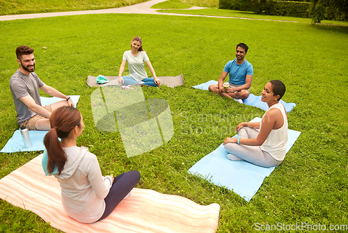 Image of group of people sitting on yoga mats at park