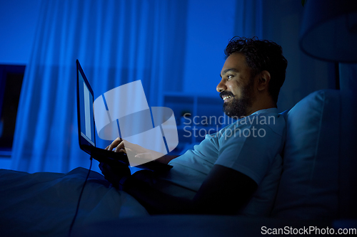 Image of indian man with laptop in bed at home at night
