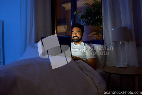 Image of indian man with laptop in bed at home at night