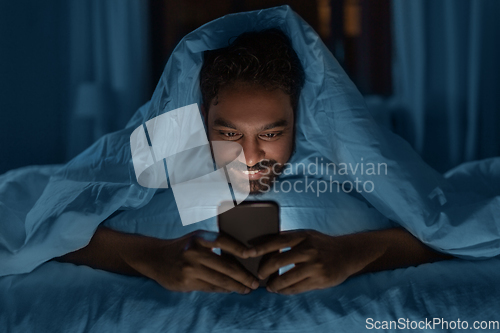 Image of indian man with smartphone in bed at home at night