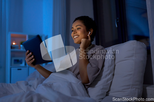 Image of woman with tablet pc in earphones in bed at night