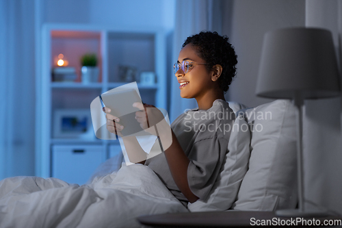 Image of woman with tablet pc in bed at home at night