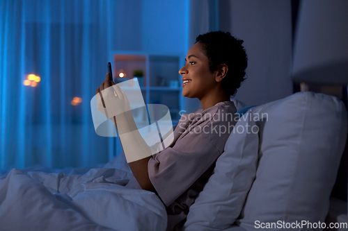 Image of woman with smartphone in bed at home at night