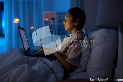 Image of woman with laptop in bed at home at night