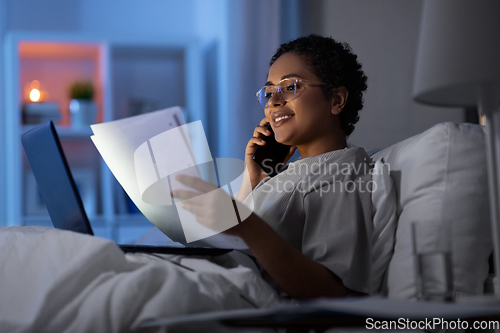 Image of woman with papers calling on phone in bed at night