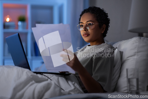 Image of woman with laptop and papers in bed at night