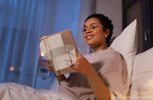 Image of smiling young woman reading book in bed at home