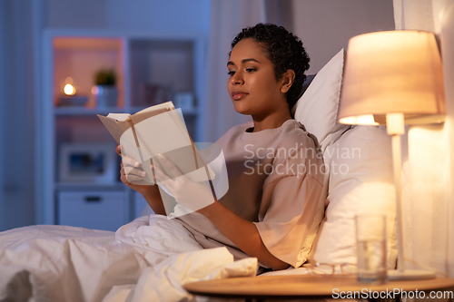 Image of young woman reading book in bed at home