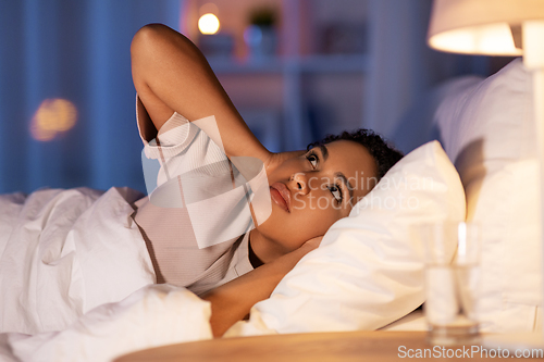 Image of angry african woman lying in bed and closing ears