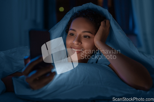Image of woman with smartphone under duvet in bed at night