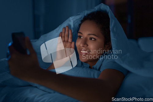 Image of woman with phone having video call in bed at night