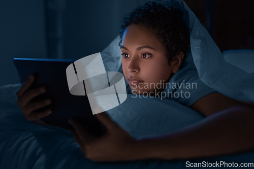 Image of woman with tablet pc under duvet in bed at night