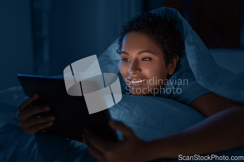 Image of woman with tablet pc under duvet in bed at night