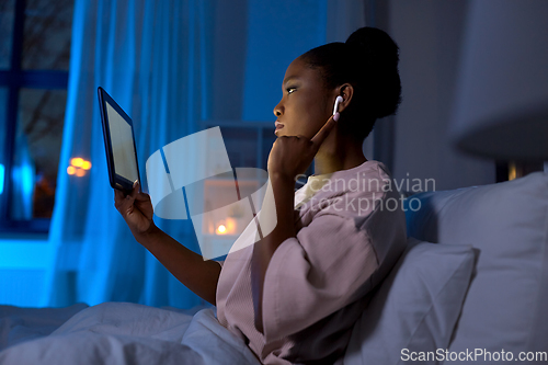 Image of woman with tablet pc in earphones in bed at night