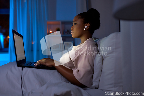 Image of woman with laptop and earphones in bed at night