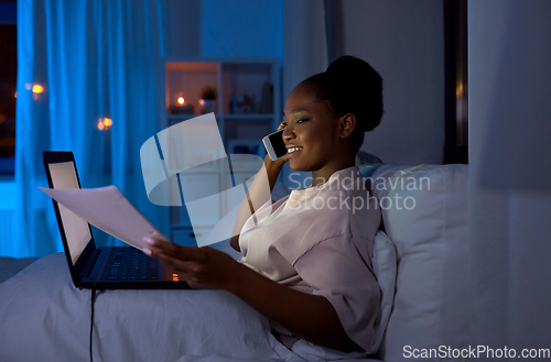 Image of woman with papers calling on phone in bed at night