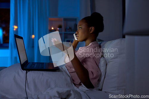 Image of woman with laptop calling on phone in bed at night