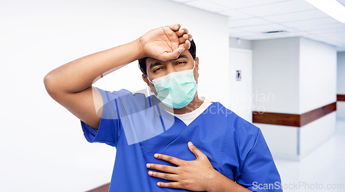 Image of tired indian male doctor in blue uniform and mask