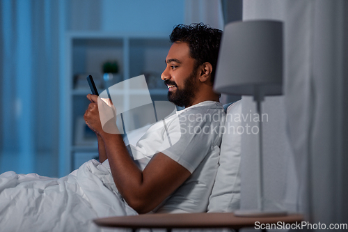 Image of indian man with smartphone in bed at home at night