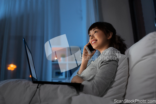 Image of woman with laptop calling on phone in bed at night