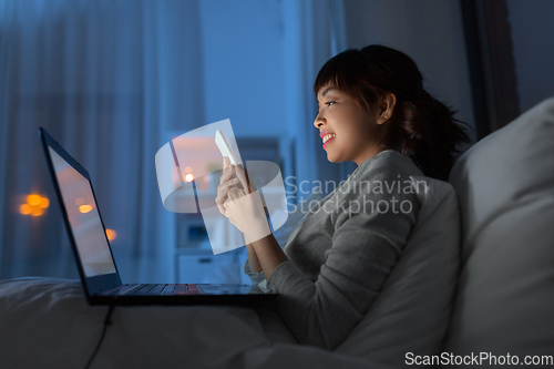 Image of asian woman with smartphone in bed at night