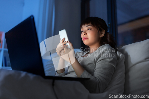 Image of asian woman with smartphone in bed at night