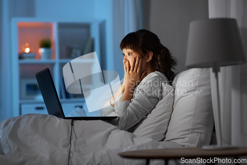 Image of stressed woman with laptop working in bed at night