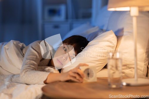 Image of asian woman with clock lying in bed at night