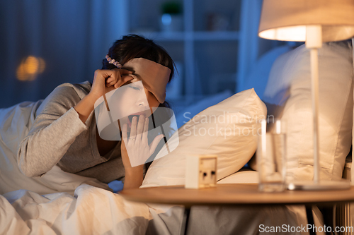 Image of asian woman with clock yawning in bed at night