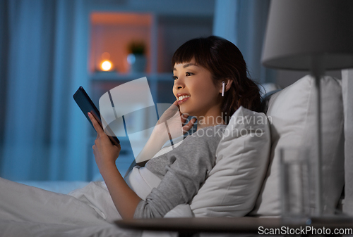 Image of woman with tablet pc in earphones in bed at night