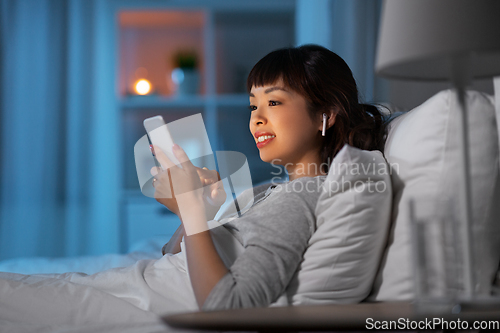 Image of woman with phone and earphones in bed at night